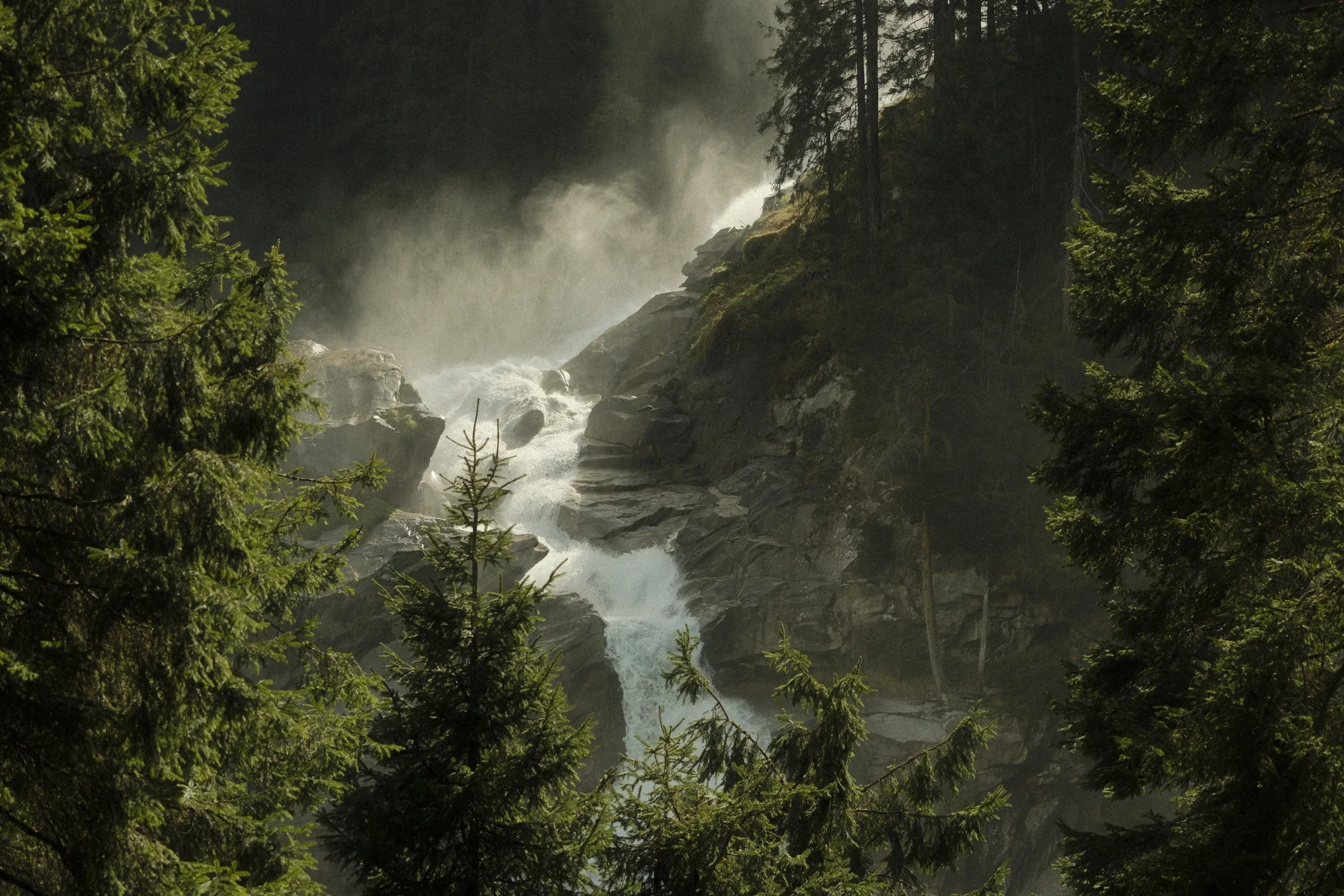 A waterfall breaking through a dark green forest in bright mist